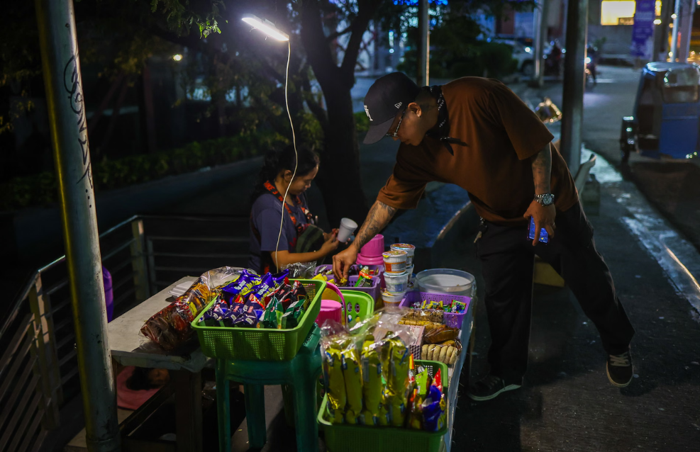 A street vendor in Manila switches on a portable, charger-powered LED light while selling his goods following the declaration of a national energy emergency in the Philippines. (Anadolu / Getty)