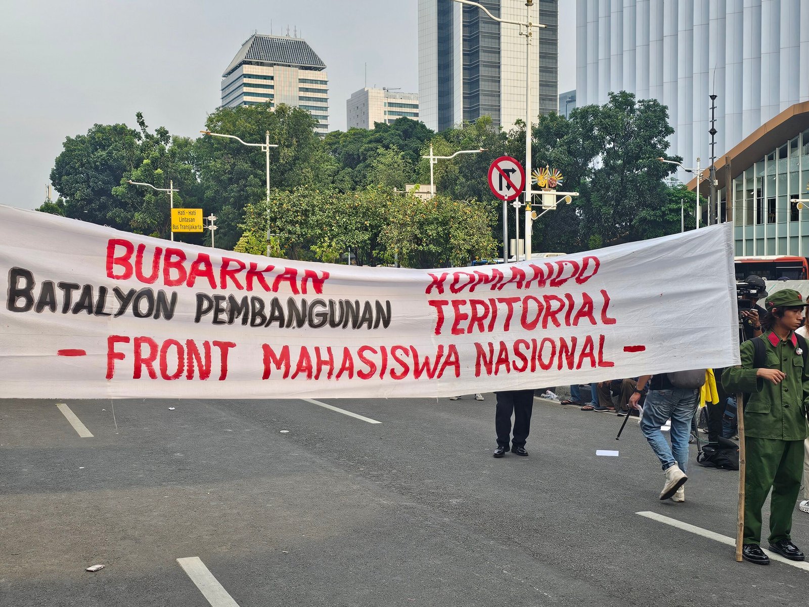 Protest banner opposing TNI military districts, created by the National Student Front, with a student dressed as a Maoist cadre on the far right. (Wikimedia)